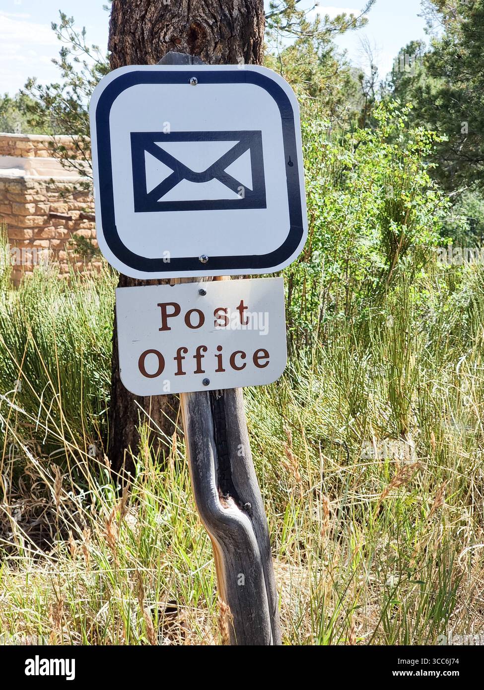 Cartello dell'ufficio postale con testo e lettera icona / pittogramma su un palo curvo in un'area rurale con alberi e erba alta Foto Stock