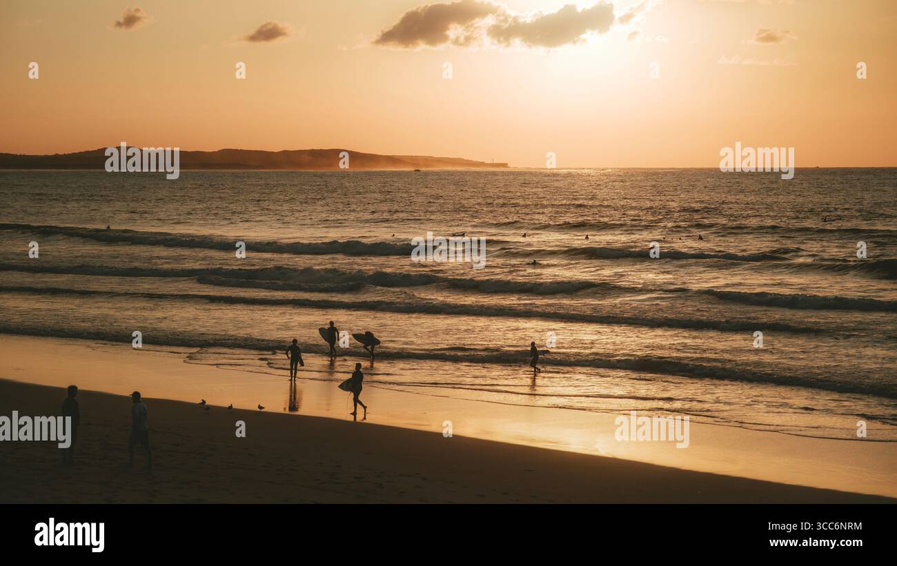 Alba sulla spiaggia di Sydney Cronulla con splendide nuvole, surfisti che portano tavole da surf sulla spiaggia all'alba, silhouette contro l'alba sulla spiaggia Foto Stock
