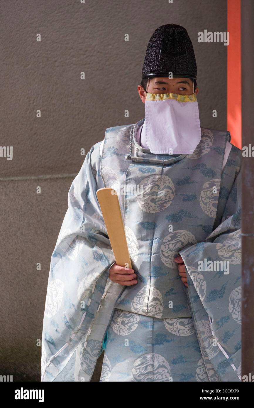 Un uomo vestito con abiti tradizionali giapponesi con un elaborato abito e copricapo tiene una pagaia di legno. L'abbigliamento culturale e l'ambiente evocano lo storico Foto Stock