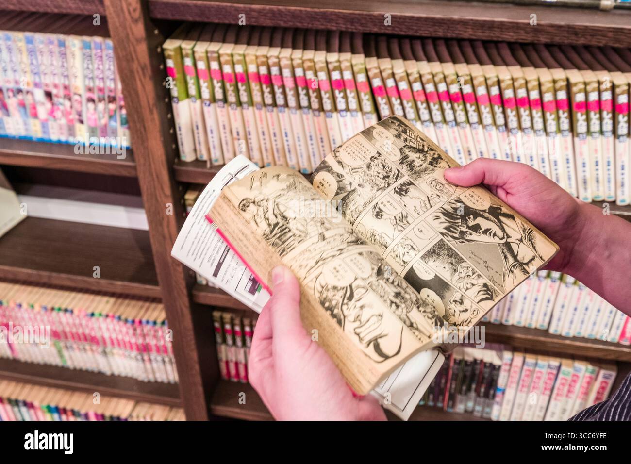 Una persona esamina un libro manga in una libreria ben fornita. La scena trasmette un senso di esplorazione, fascino e interesse culturale in Japanese com Foto Stock