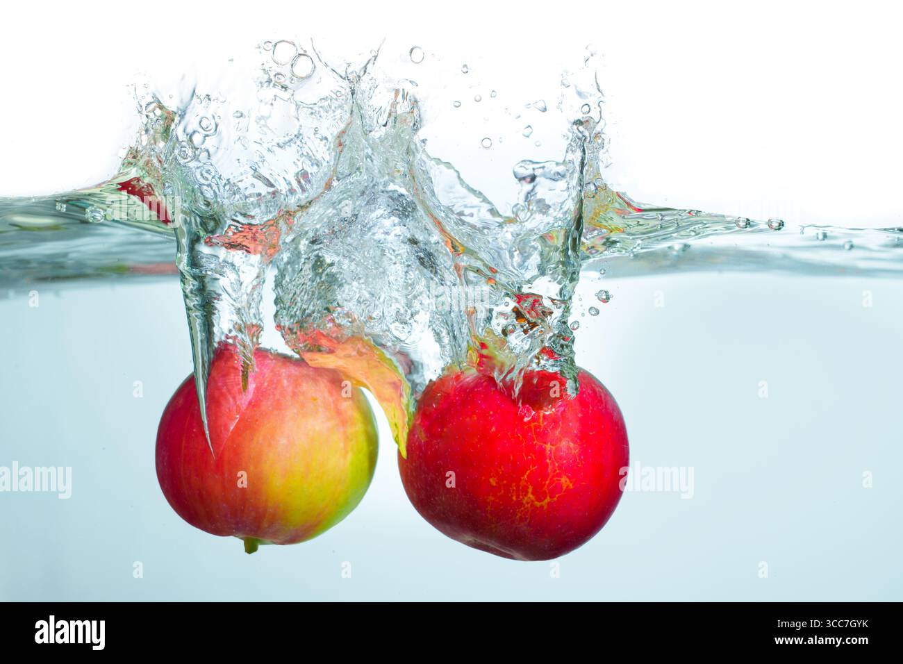Spruzzi dinamici di due mele rosse che colpiscono la superficie dell'acqua, creando bolle e increspature in un ambiente di acqua limpida. Foto Stock