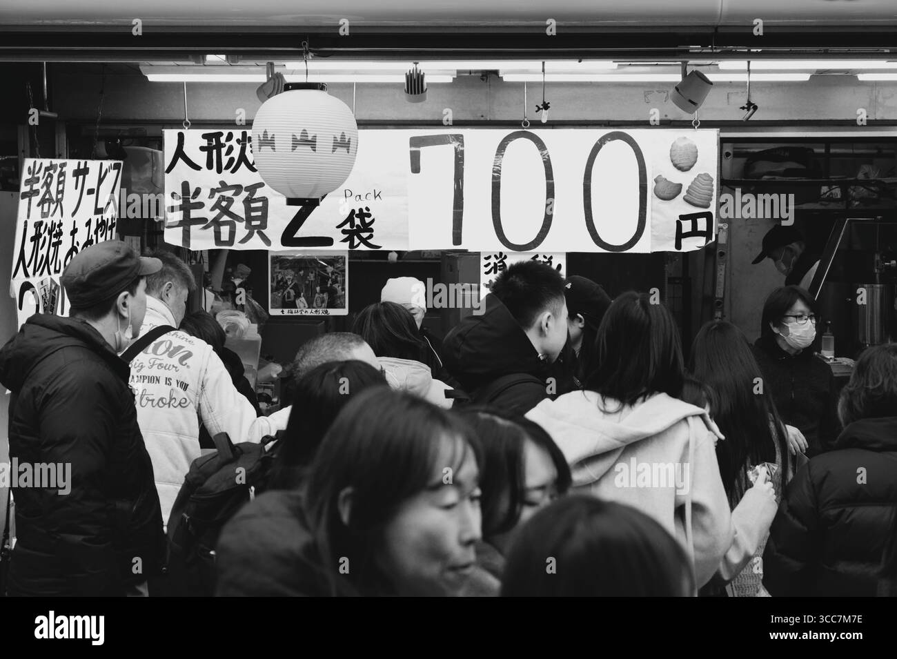 La folla si riunisce di fronte a una bancarella di merci scontate nella via dello shopping Nakamise in bianco e nero Foto Stock
