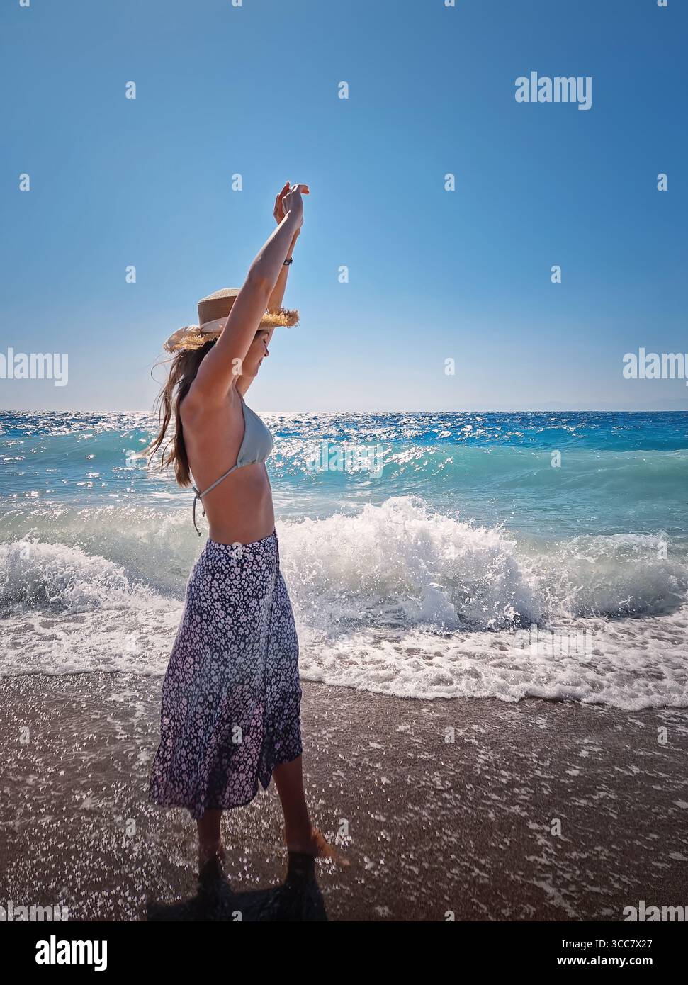 Vista laterale la bella donna si staglia spensierata tra le onde spumeggianti del mare azzurro, di fronte all'ampio orizzonte sotto un cielo estivo senza nuvole. Estate V Foto Stock
