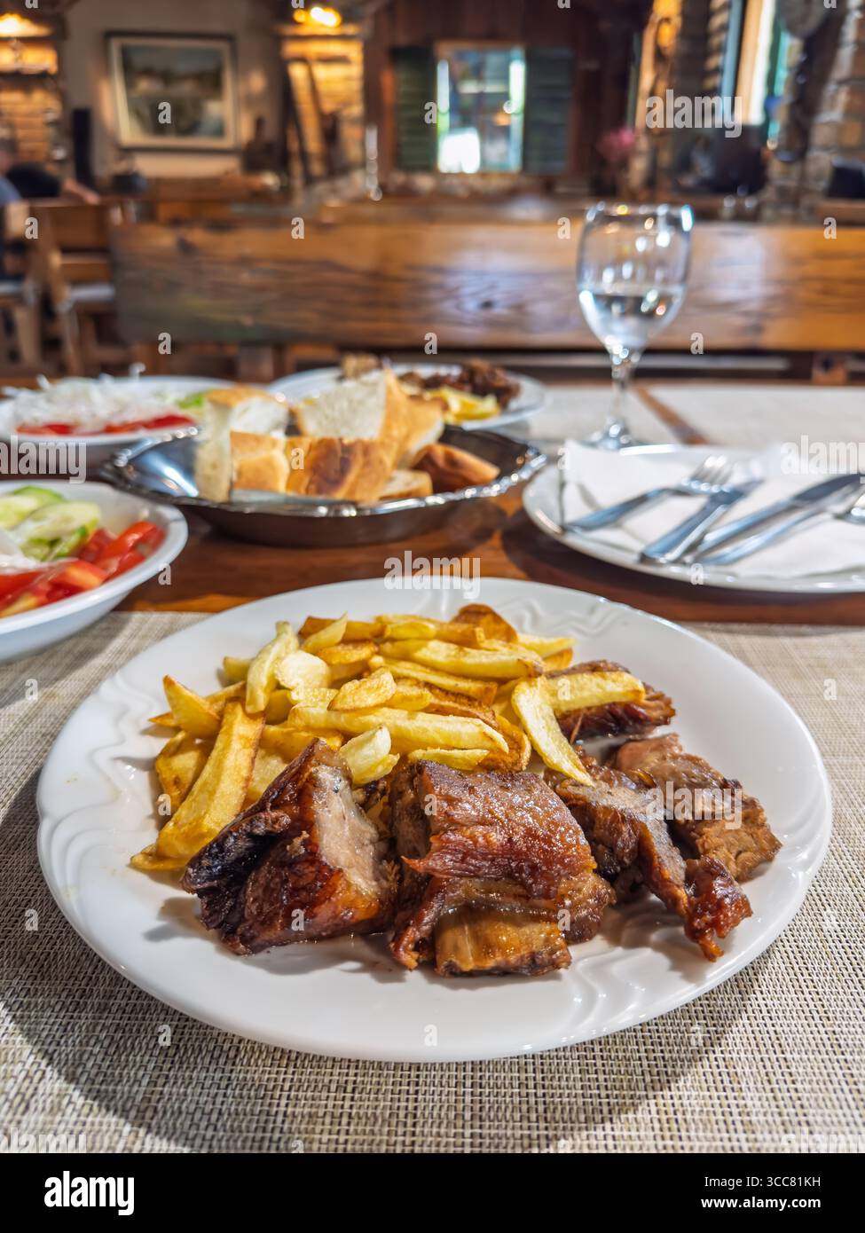 Cena in un konoba croato. L'attenzione e' su un delizioso piatto di carne arrosto, che mostra i ricchi sapori della cucina Mediterranea. Un pasto soddisfacente Foto Stock