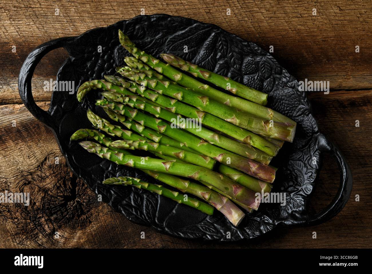 Un piatto nero ripieno di lance di asparagi appena raccolte, su un tavolo in legno rustico. Foto Stock