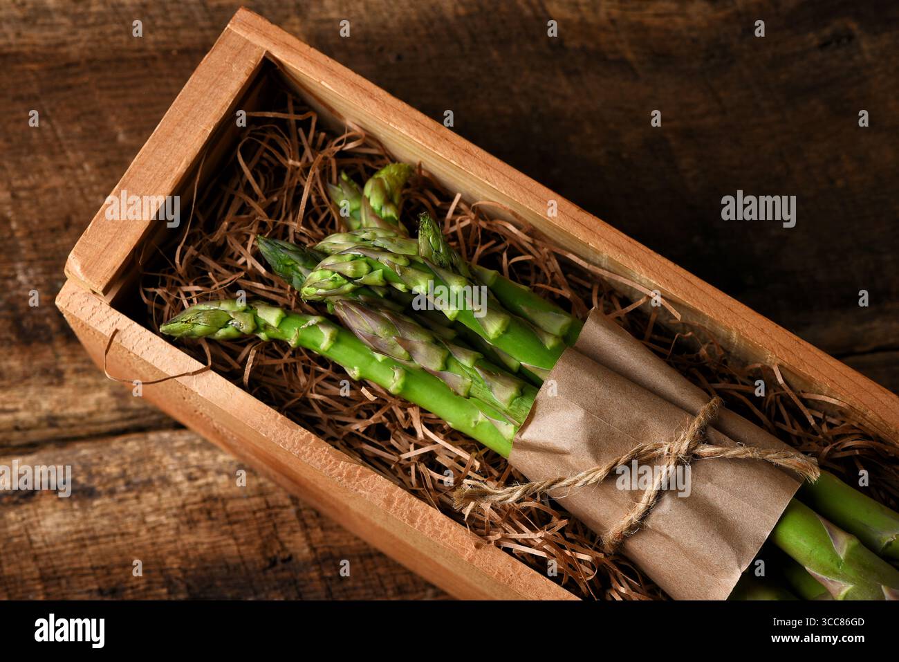 Una cassa di legno con paglia da imballaggio e un mazzo di asparagi con carta e spago. Foto Stock