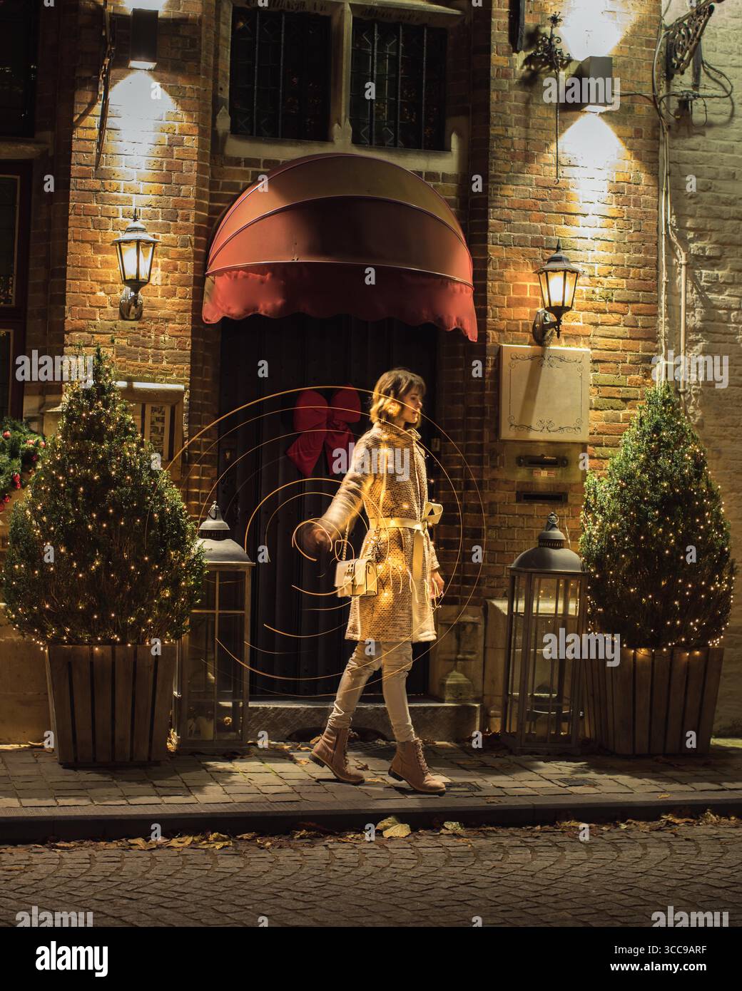 Bella giovane donna in piedi lateralmente di fronte all'ingresso dell'edificio, mentre si fanno le tracce di luce che si muovono e girano le luci nelle mani. Foto Stock