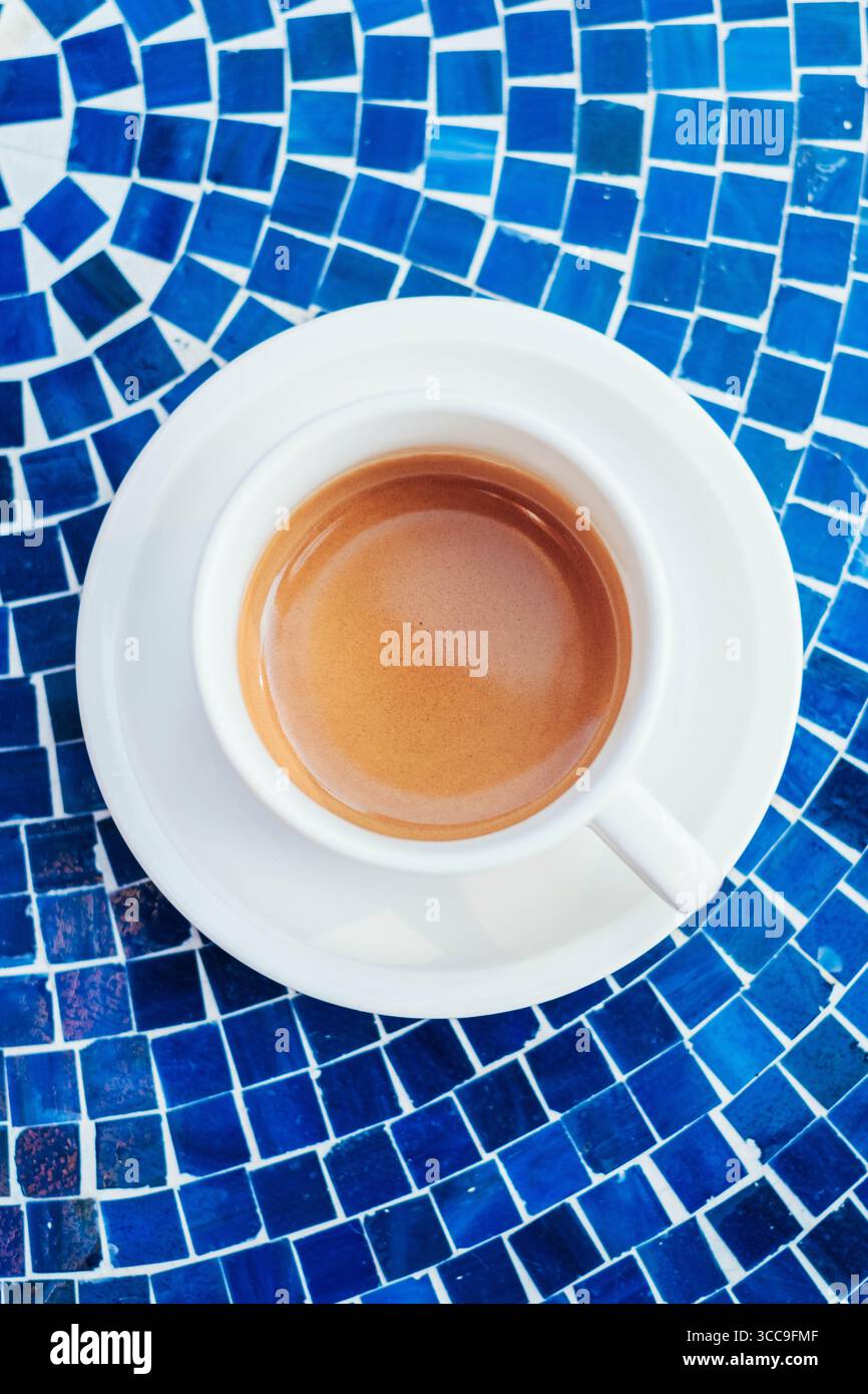Espresso appena estratto in tazza bianca sul tavolo con mosaico blu Foto Stock