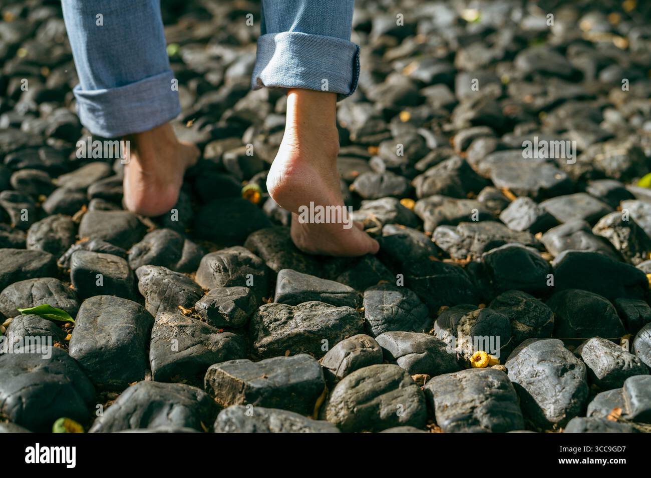 Primo piano di una donna a piedi nudi che cammina su un terreno di ghiaia in un tranquillo rifugio nella foresta durante la luce del mattino presto. Cura di sé, guarigione emotiva e connessione Foto Stock