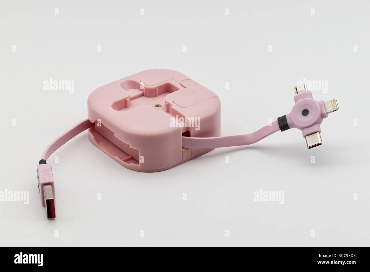 Un cavo di ricarica multipla retrattile rosa con vari connettori si trova su uno sfondo bianco pulito, pronto per l'uso. Foto Stock