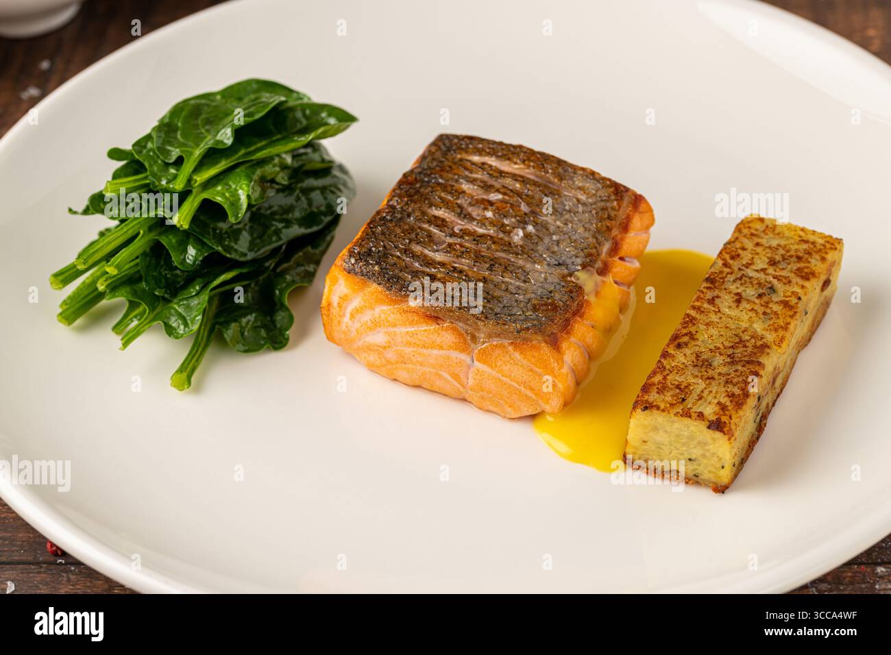 Filetto di salmone scottato servito con spinaci saltati e croquette di patate Foto Stock