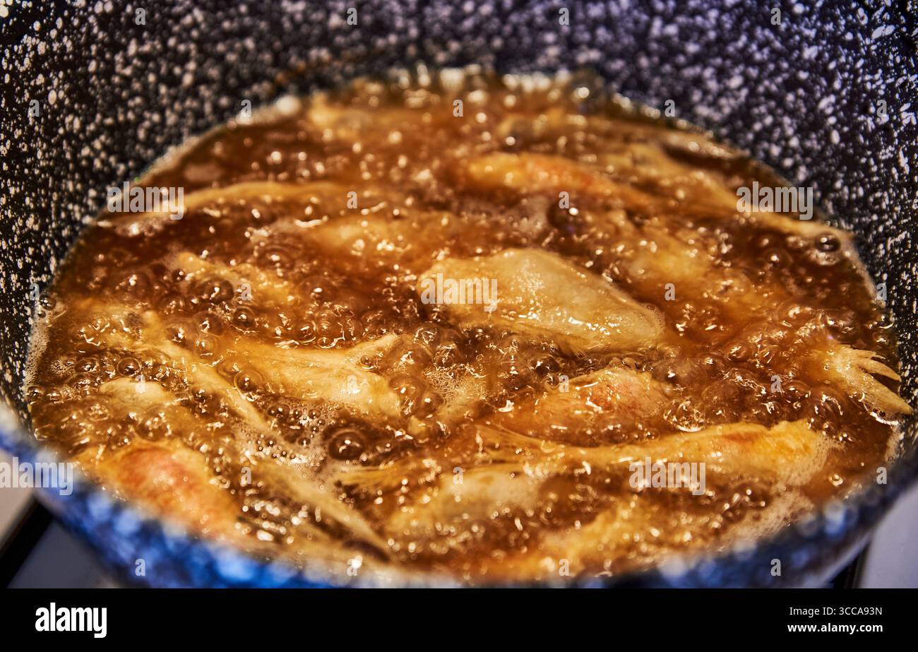 Il piccolo pesce dorato si mescola in olio caldo, catturando una tradizione rustica del sud dell'Italia. Croccante in una padella macchiata, questa scena rispecchia il passato Foto Stock