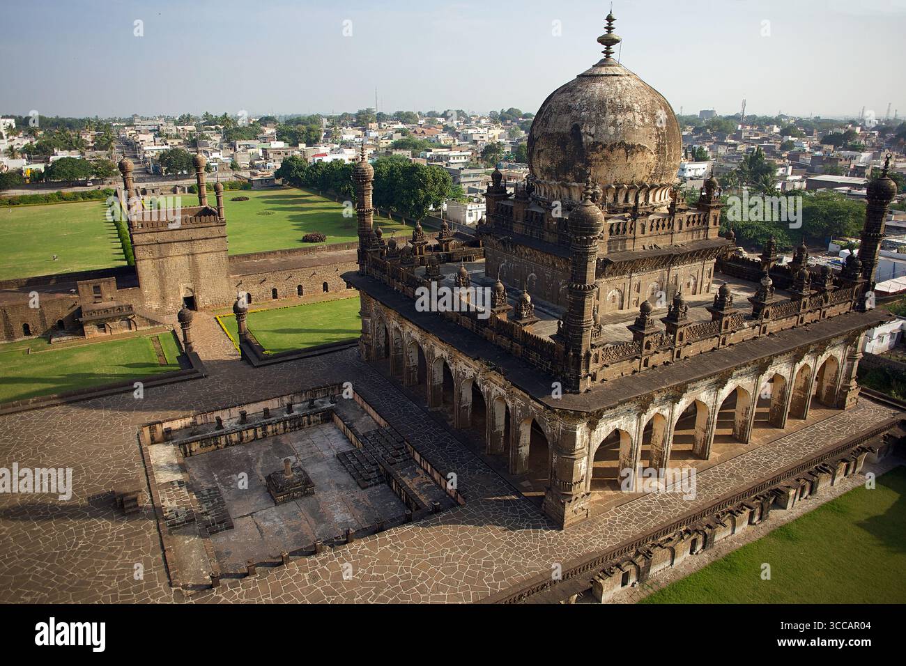 Vista aerea delle intricate pietre di Ibrahim Rauza bagnate dal caldo bagliore del sole, contrastando con i lussureggianti prati verdi e la lontana città di Bijapur, Karnataka, India. Foto Stock
