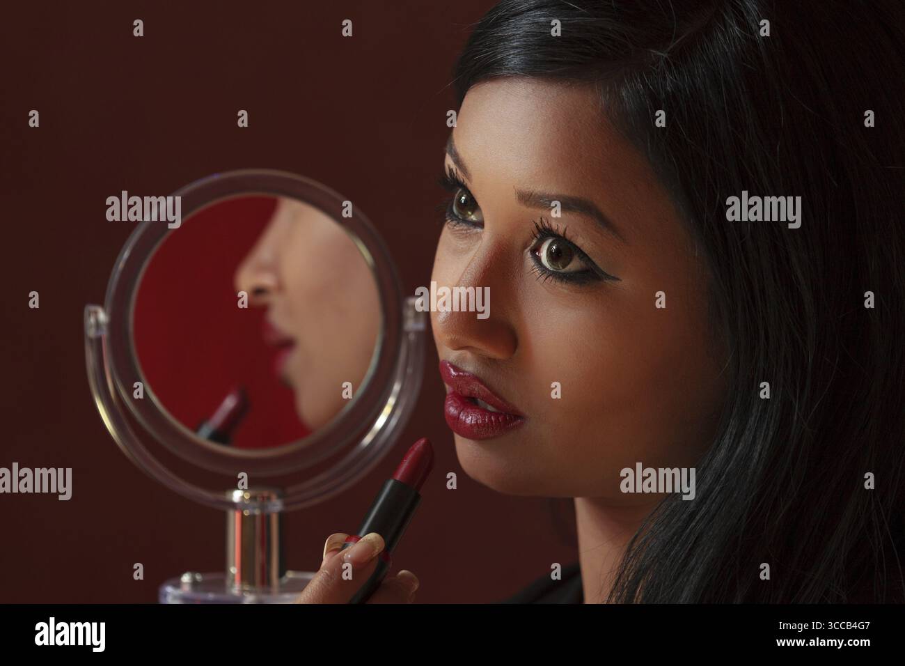 Pretty Woman dall'aspetto asiatico applica il rossetto rosso e guarda il suo riflesso, enfatizza l'eleganza e la fiducia in se stessi, scatta ritratti, studio Foto Stock