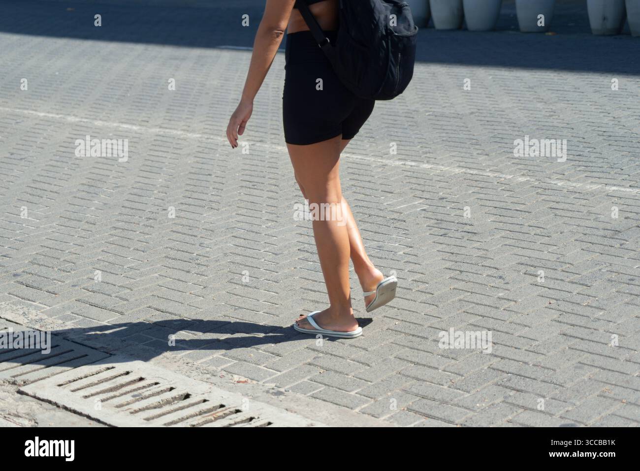 Parte inferiore di una persona non identificata che cammina su un marciapiede della strada durante la forte luce del sole. Attività, direzione, percorso. Foto Stock