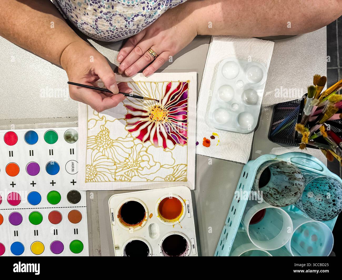 Vista dall'alto della donna che dipinge con cura intricati motivi floreali di Batik utilizzando colori vivaci in uno spazio di lavoro creativo. kuala lumpur, malesia - Immagine stock catturata con smartphone