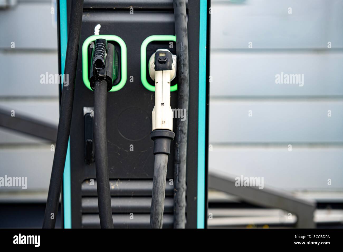 Stazione di ricarica per veicoli elettrici con due connettori: Primo piano dei cavi e delle prese di alimentazione EV moderni con linee LED verdi sul pannello nero Foto Stock