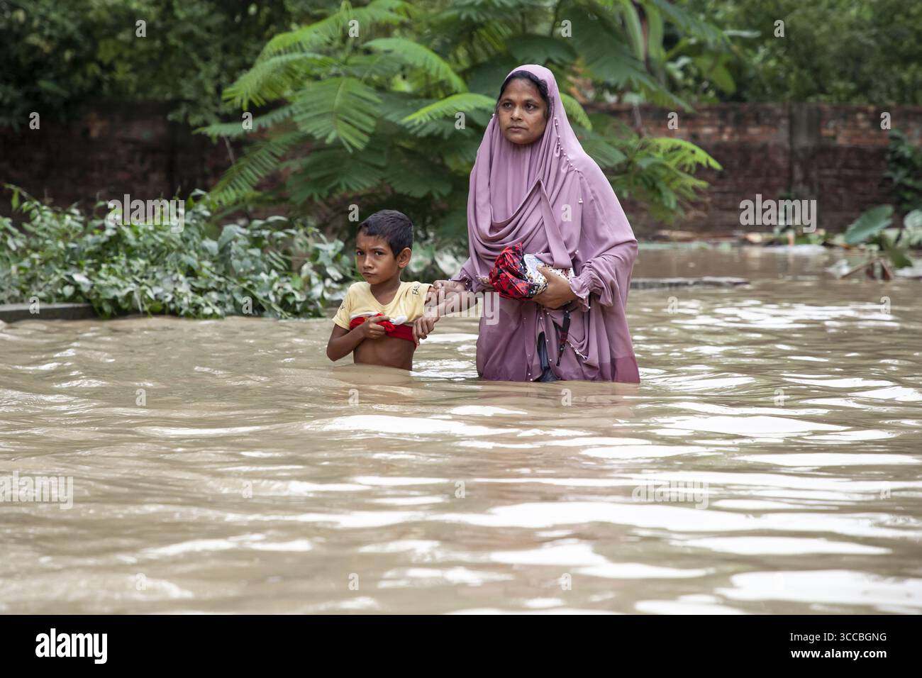 Satkania, Bangladesh - 09 agosto 2023: Visione di una madre e di un bambino che attraversano le acque alluvionali, le loro espressioni riflettono la resilienza tra le profondità torbide. Foto Stock