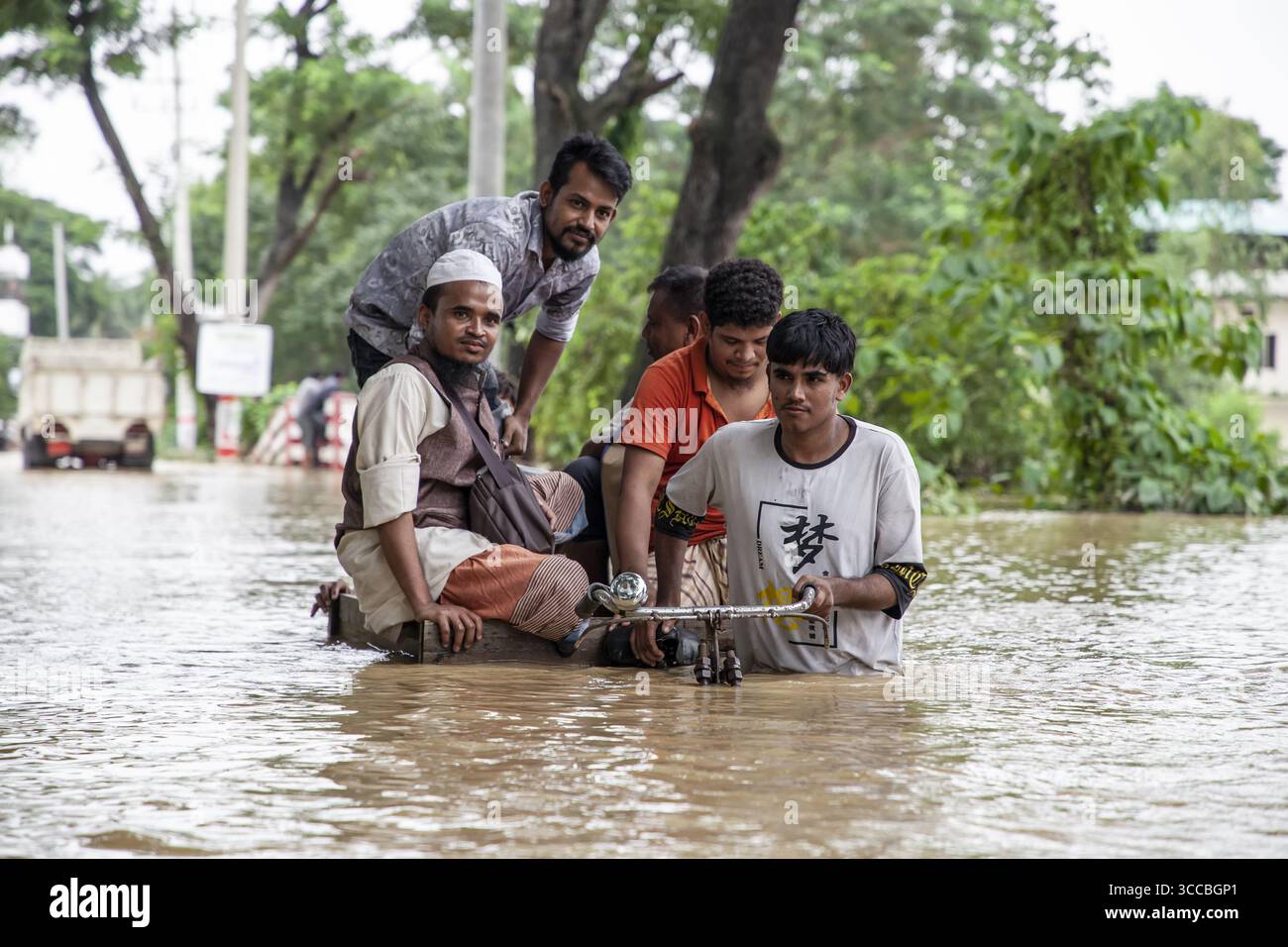 Satkania, Bangladesh - 09 agosto 2023: Vista delle acque alluvionali che inondano le strade, riflettendo il cielo coperto mentre gli uomini navigano nel diluvio, spingendo una bicicletta attraverso le profondità torbide. Foto Stock