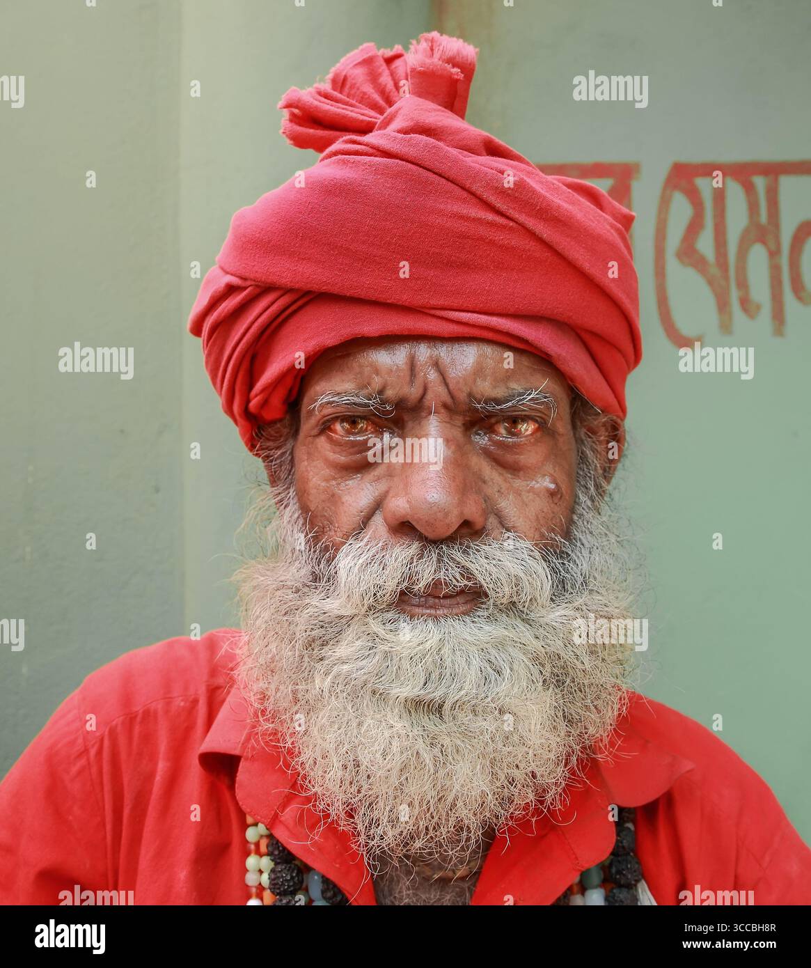 Chandanath Hill, Bangladesh - 12 marzo 2021: Veduta di un uomo anziano con un sorprendente turbante rosso e un volto intemprato, il suo sguardo intenso ammorbidito di un lungo Foto Stock