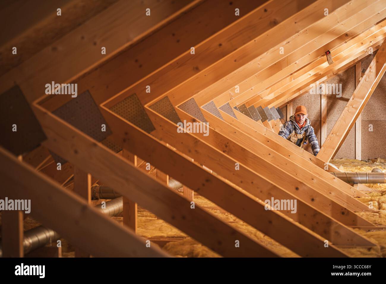 Un operaio edile controlla i materiali isolanti in un sottotetto in legno con travi esposte e una disposizione ordinata degli elementi strutturali. Foto Stock