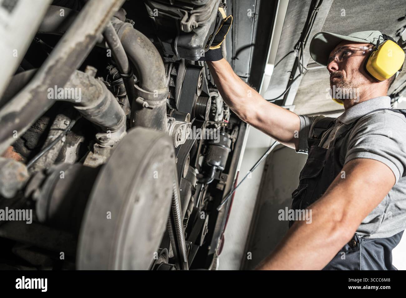 Un meccanico esperto esamina il funzionamento interno di macchinari pesanti in una vivace officina industriale durante il giorno, garantendo il corretto funzionamento e la sicurezza Foto Stock