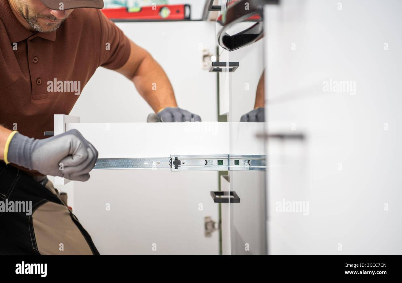 Un professionista sta installando cassetti scorrevoli in un armadietto in una cucina contemporanea. L'attività richiede attenzione ai dettagli e precisione per la funzionalità Foto Stock