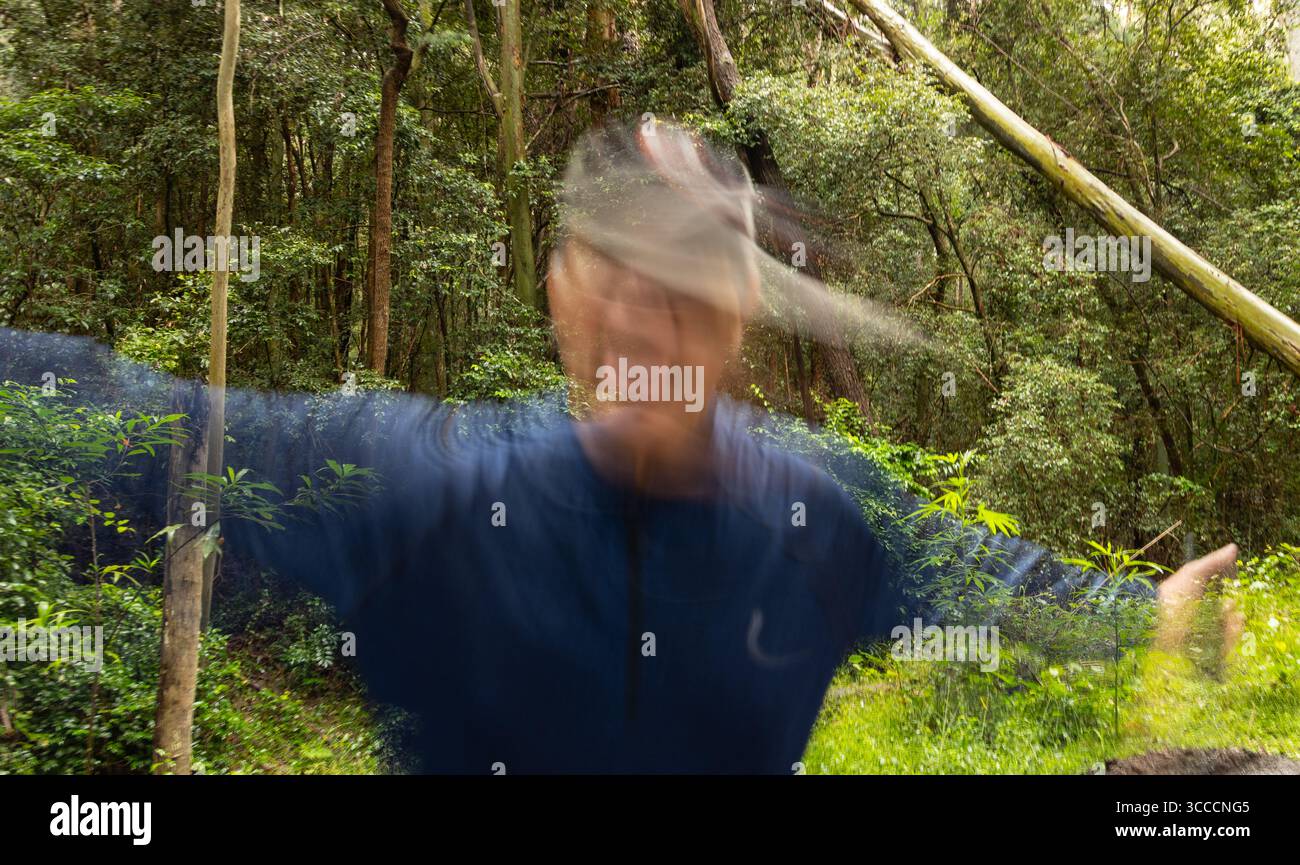 Immagine sfocata di una persona con una camicia blu e un cappello che gira in una foresta. La sfocatura del movimento suggerisce che si stanno muovendo rapidamente. Foto Stock