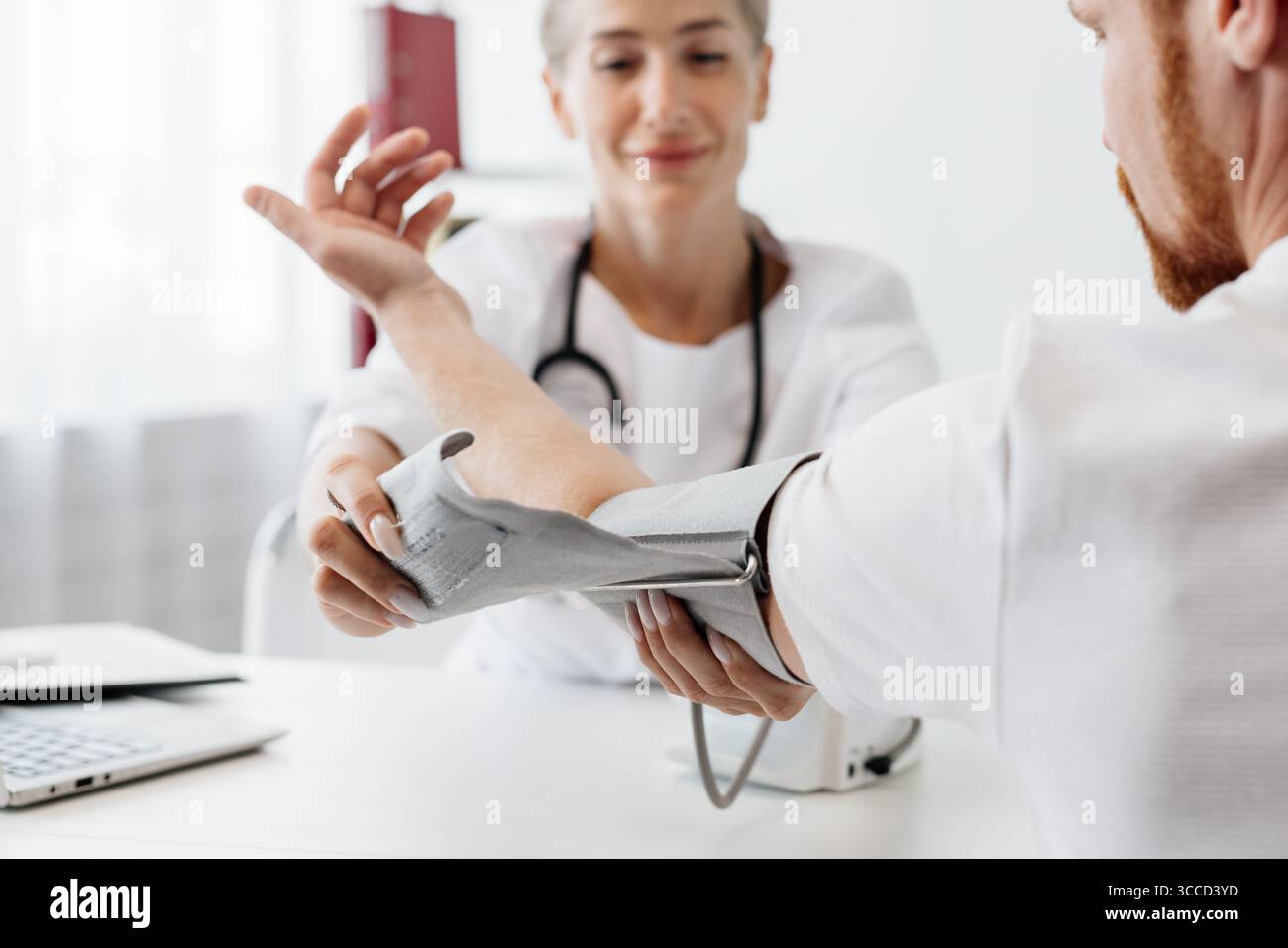 Il medico femminile misura la pressione sanguigna di un paziente di sesso maschile in una clinica moderna, evidenziando un ambiente sanitario professionale con attrezzature mediche un Foto Stock