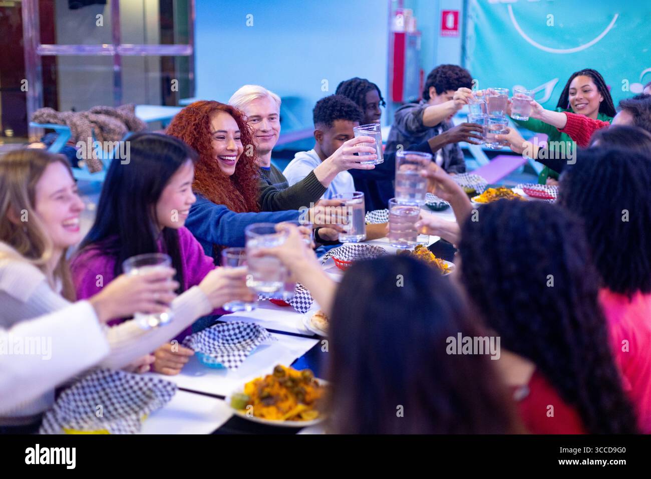 Amici multietnici felici che alzano i bicchieri d'acqua e brindano seduti a un tavolo del ristorante, festeggiando insieme Foto Stock