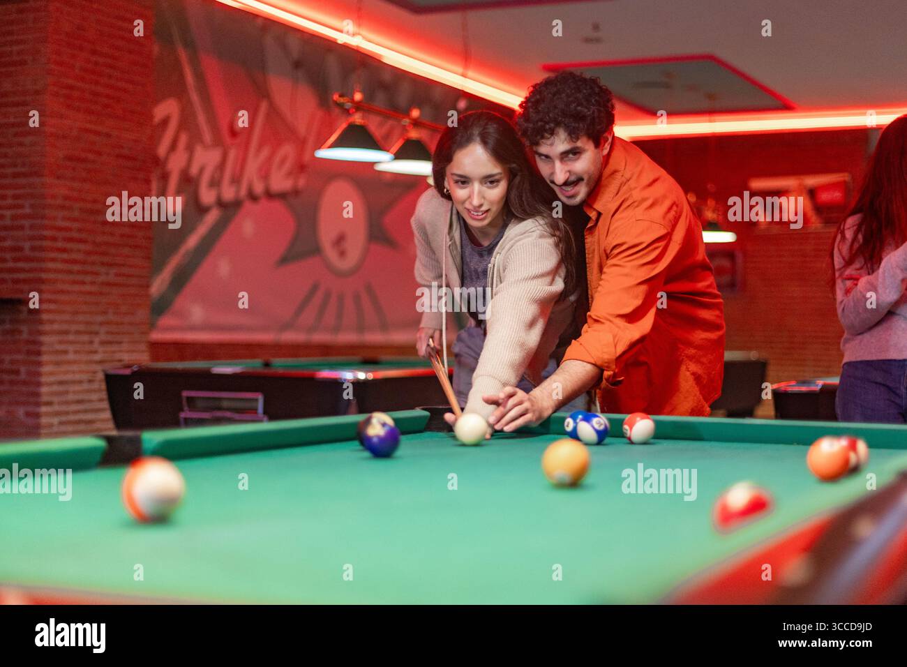 Coppia felice che si diverte con un vivace gioco di piscina in un pub elegante, circondato dal bagliore di vivaci luci al neon, creando un'atmosfera divertente Foto Stock