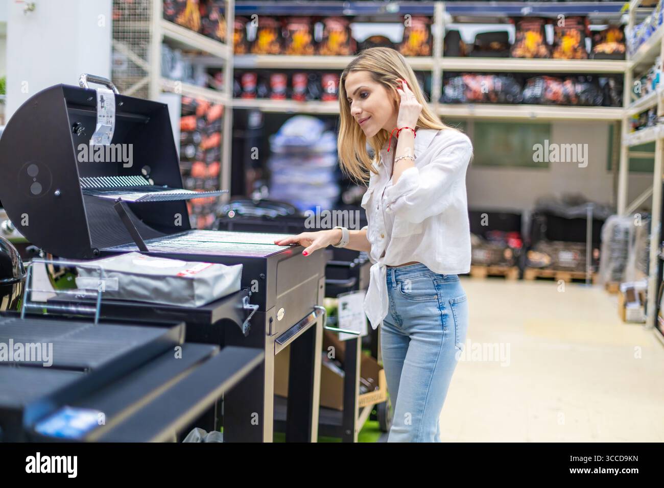 Cliente che sceglie una nuova griglia per barbecue in un negozio di ferramenta, esamina le funzioni e prende una decisione di acquisto Foto Stock