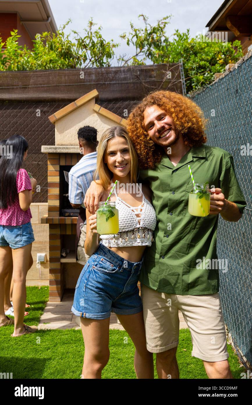 Giovani coppie che si godono una rinfrescante limonata durante una festa al barbecue sul retro con gli amici, festeggiando l'estate con buona compagnia e cibo delizioso Foto Stock