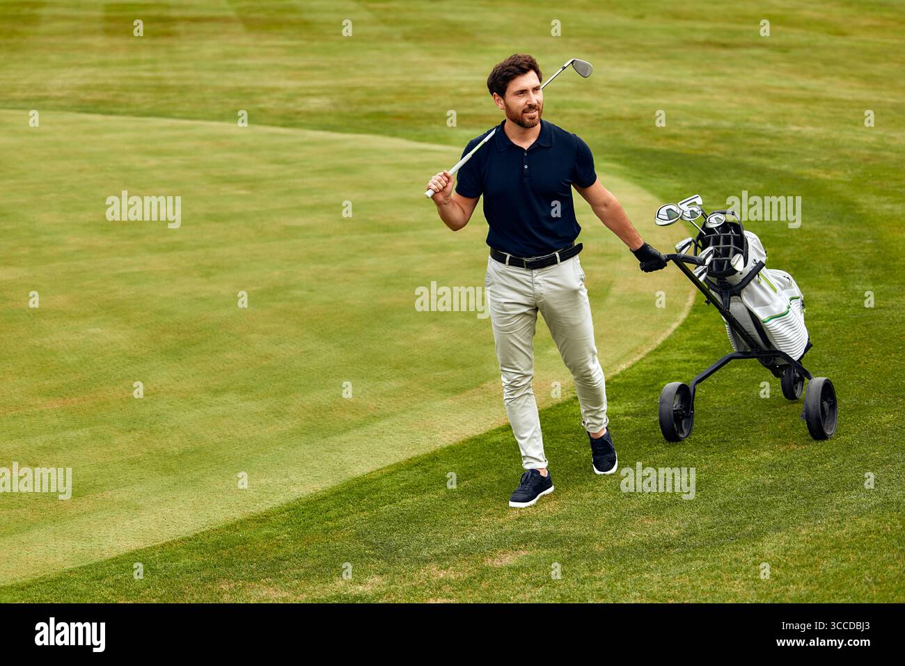 Un uomo sta passeggiando con una mazza da golf in una mano e una borsa da golf gli è sganciata sulle spalle in una giornata di sole nel vasto campo da golf, sho Foto Stock