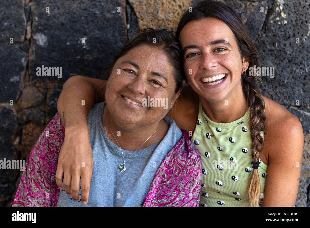 Madre e figlia felici sorridono e si abbracciano di fronte a un muro di pietra Foto Stock
