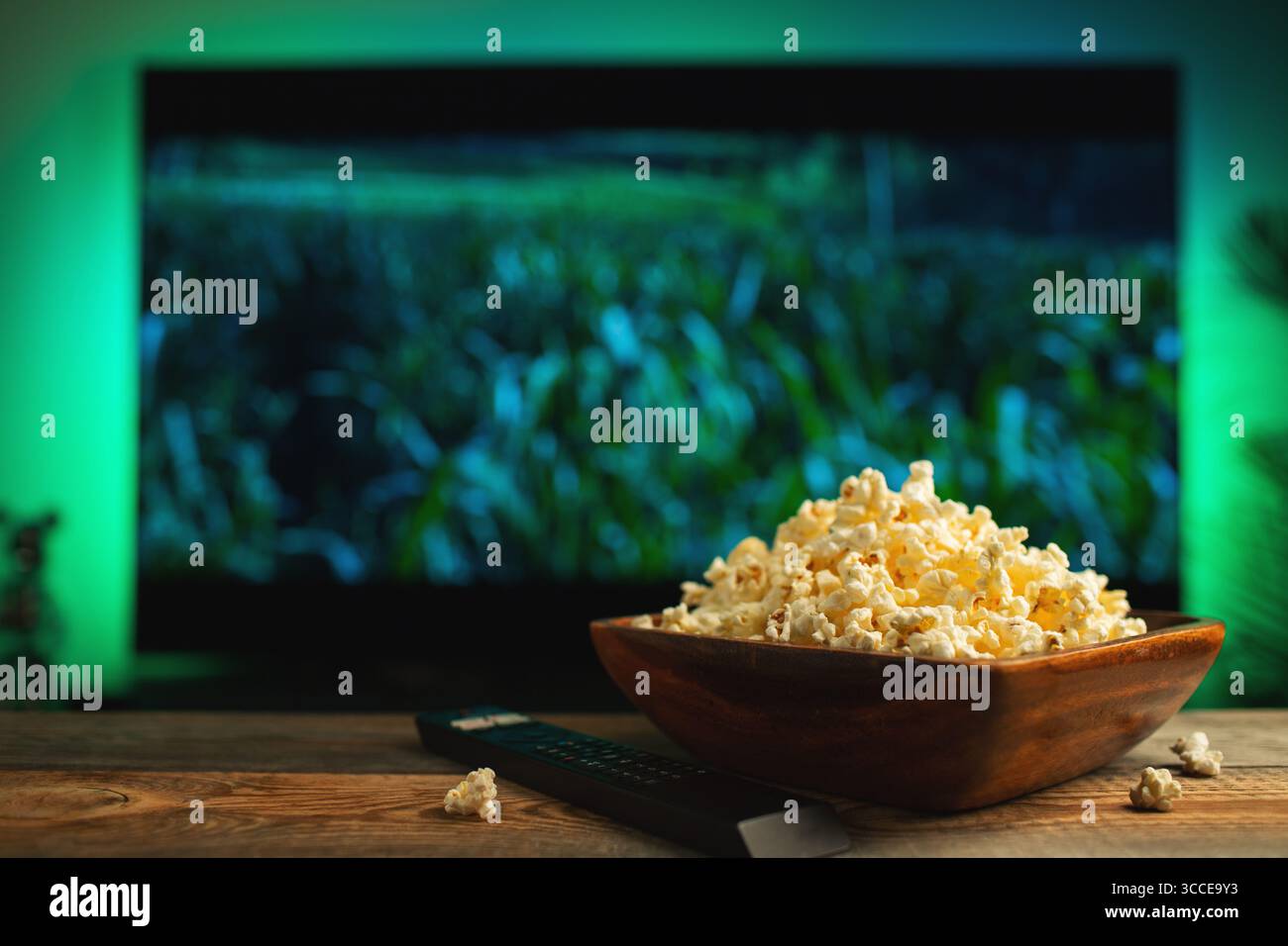 Una ciotola di popcorn in legno e telecomando sullo sfondo il televisore funziona. Serata accogliente guardando un film o una serie TV a casa. Foto Stock
