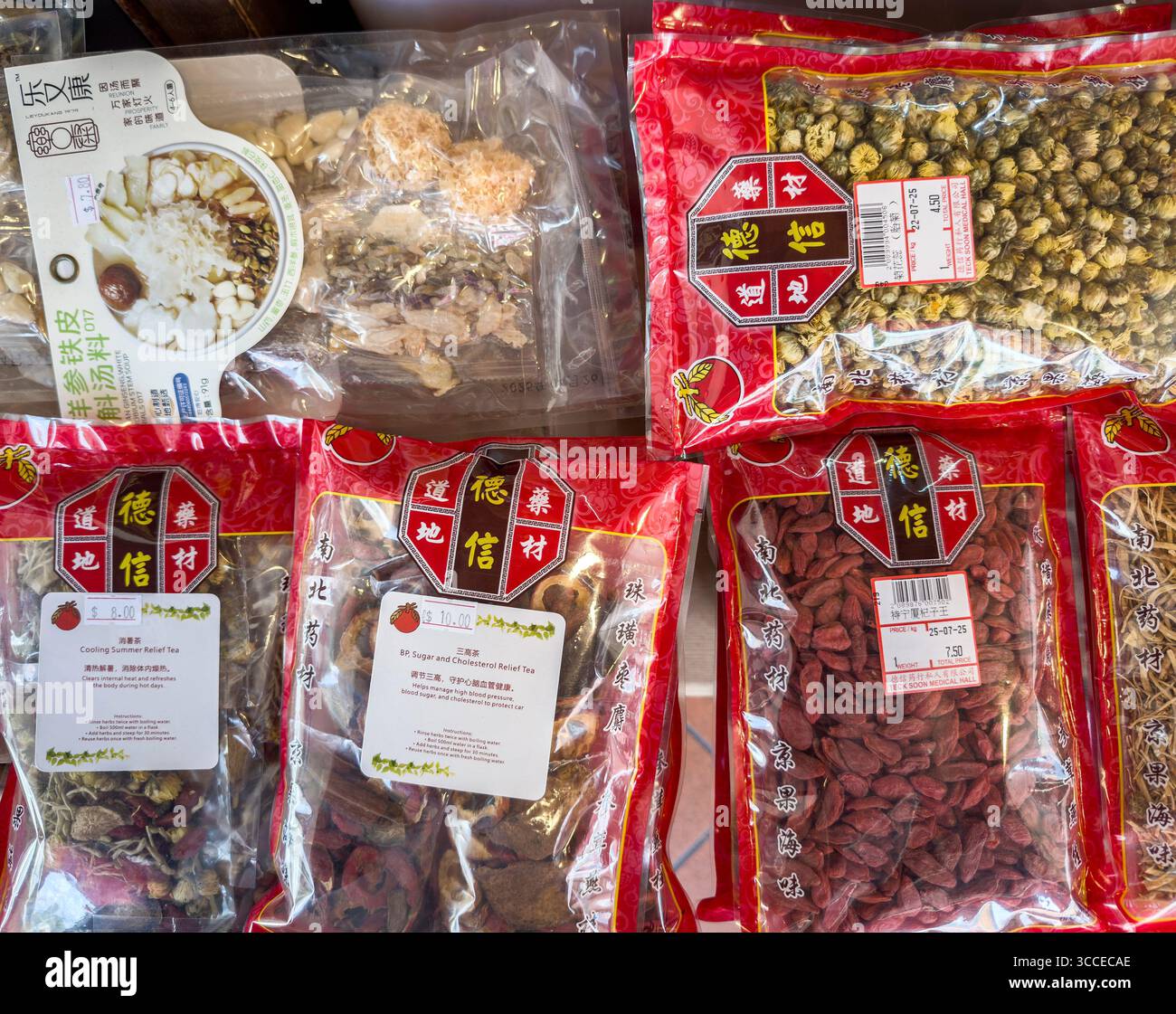 Primo piano di varie confezioni di erbe e frutta essiccate medicinali cinesi in mostra confezioni rosse vibranti e testo ed etichette cinesi nella sala medica di singapore - Immagine stock catturata con smartphone