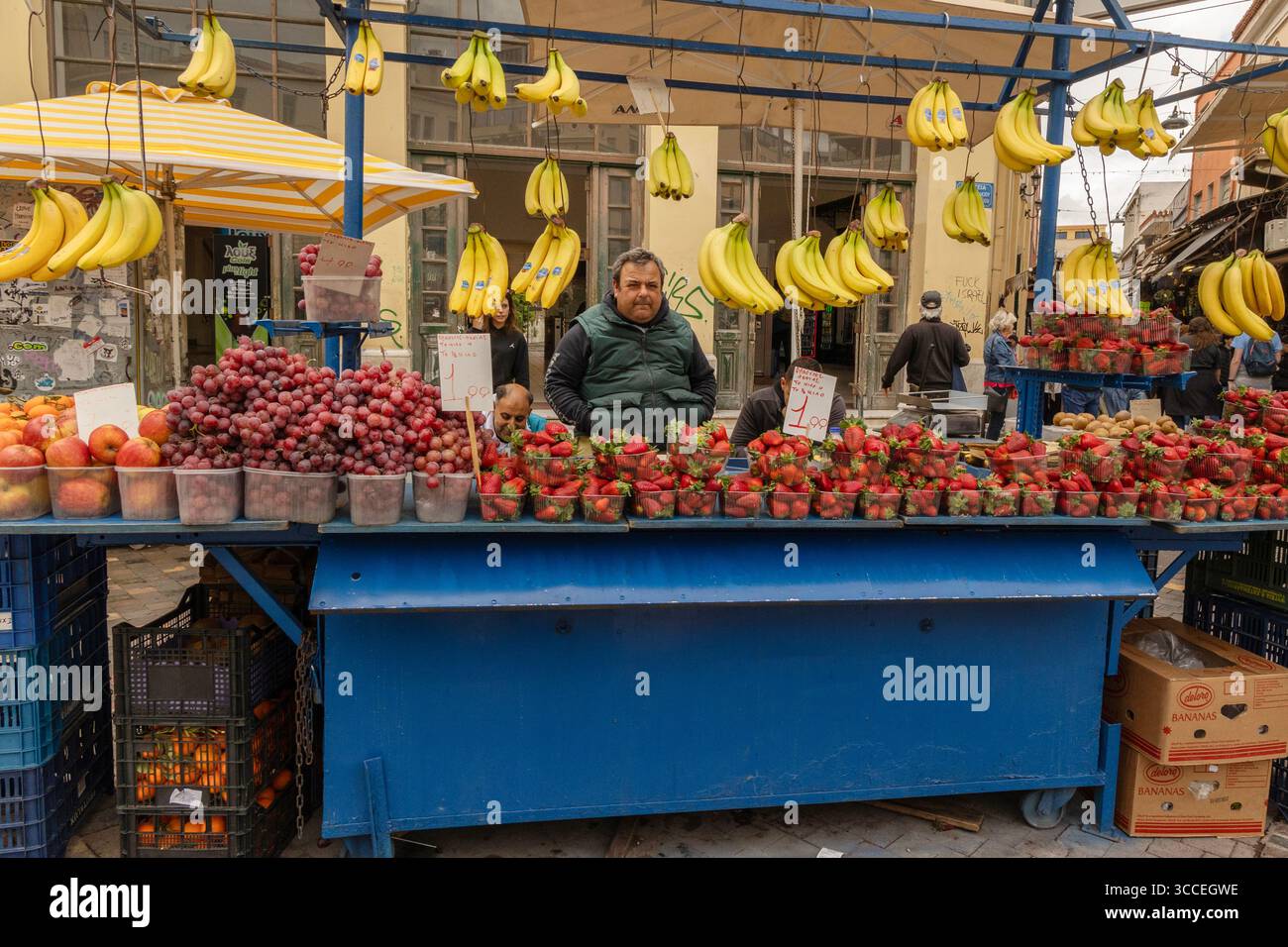 Vista a livello della strada, primo piano di un uomo che prepara frutta in una vivace bancarella di strada ad Atene, Grecia. Foto Stock