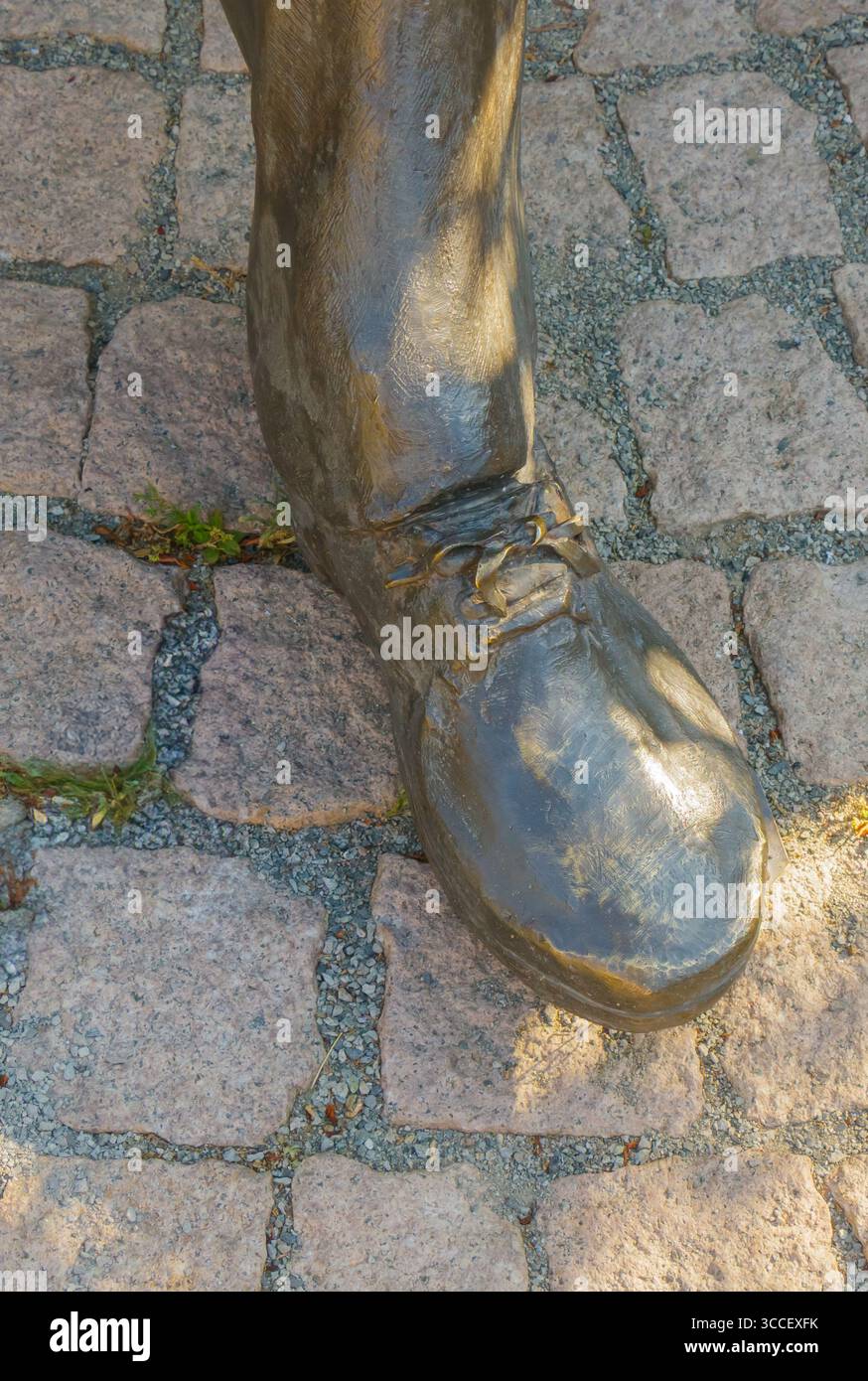 Una dettagliata scultura in bronzo di una scarpa poggia su un sentiero acciottolato, circondato dal verde, che mostra arte e artigianato in un ambiente tranquillo all'aperto Foto Stock