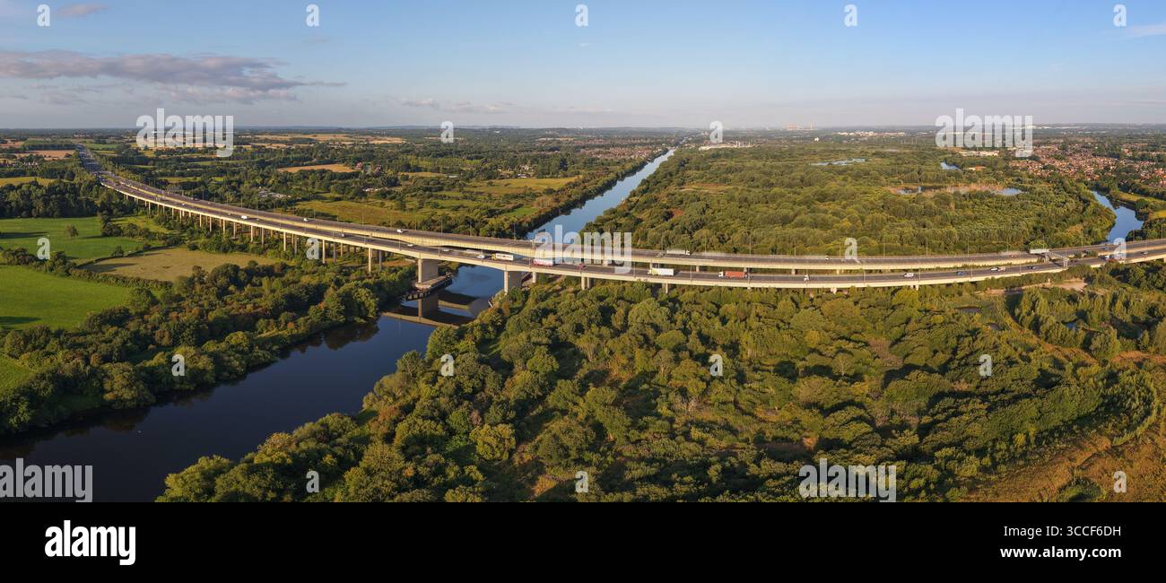 Immagine aerea dell'autostrada M6 sul viadotto di Thelwall che attraversa il fiume Mersey vicino a Warrington, con lussureggianti boschi verdi e campagna aperta Foto Stock