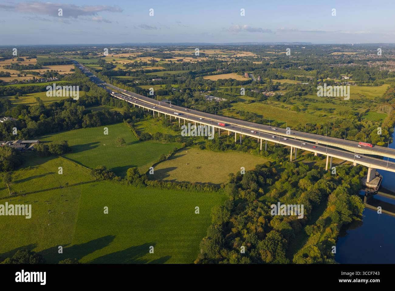 Immagine aerea dell'autostrada M6 sul viadotto di Thelwall che attraversa il fiume Mersey vicino a Warrington, con lussureggianti boschi verdi e campagna aperta Foto Stock