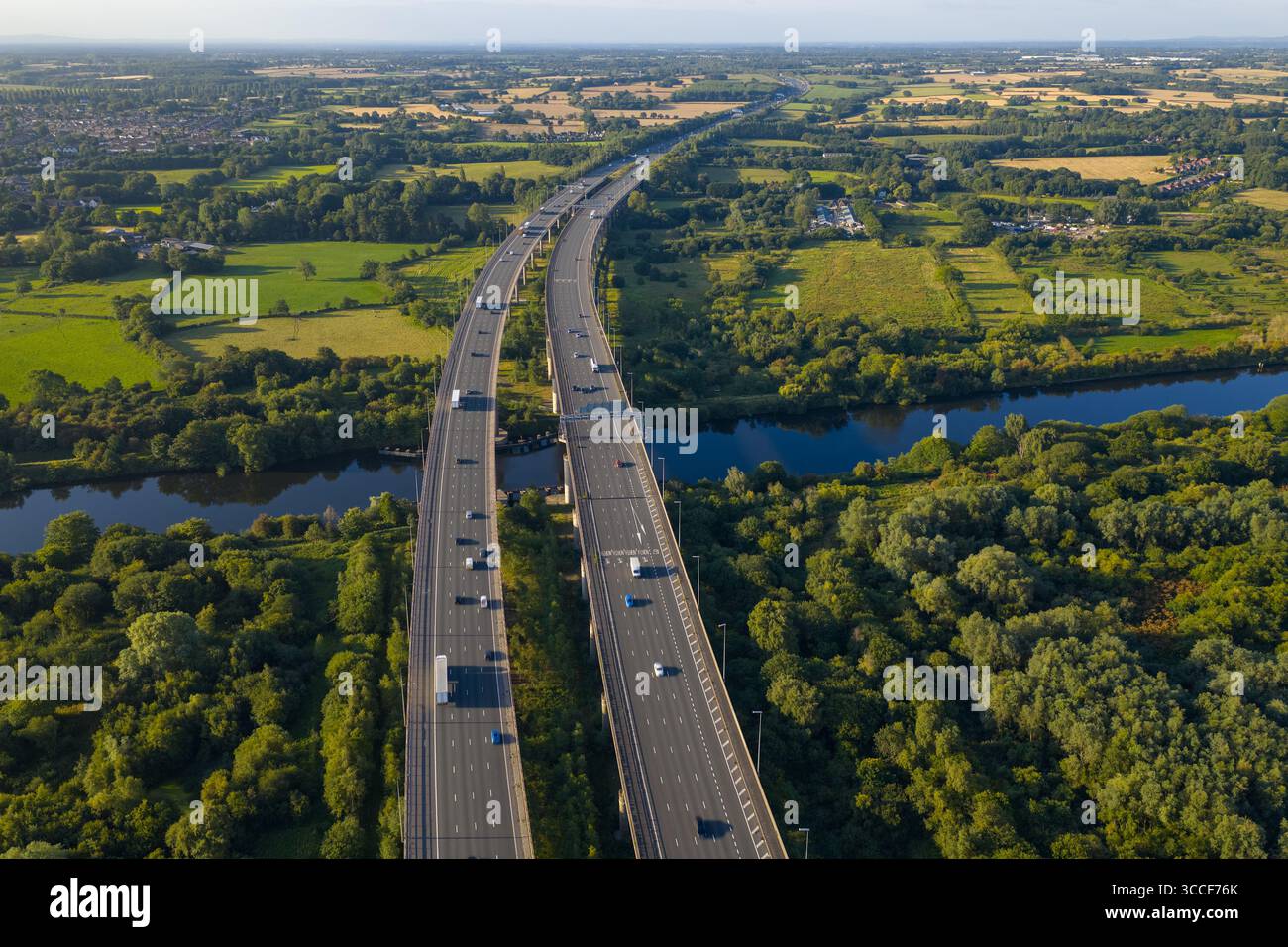 Immagine aerea dell'autostrada M6 sul viadotto di Thelwall che attraversa il fiume Mersey vicino a Warrington, con lussureggianti boschi verdi e campagna aperta Foto Stock