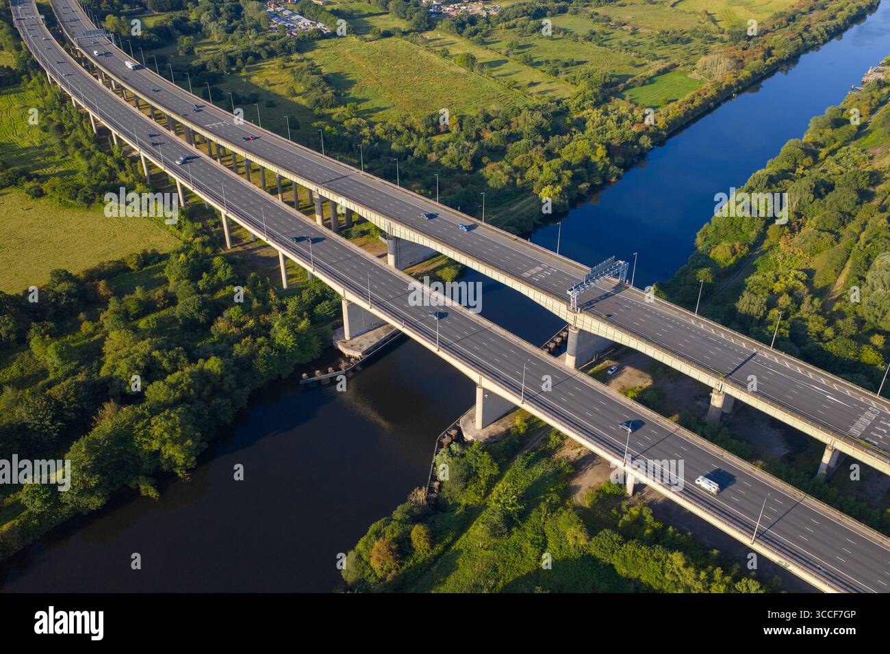 Immagine aerea dell'autostrada M6 sul viadotto di Thelwall che attraversa il fiume Mersey vicino a Warrington, con lussureggianti boschi verdi e campagna aperta Foto Stock
