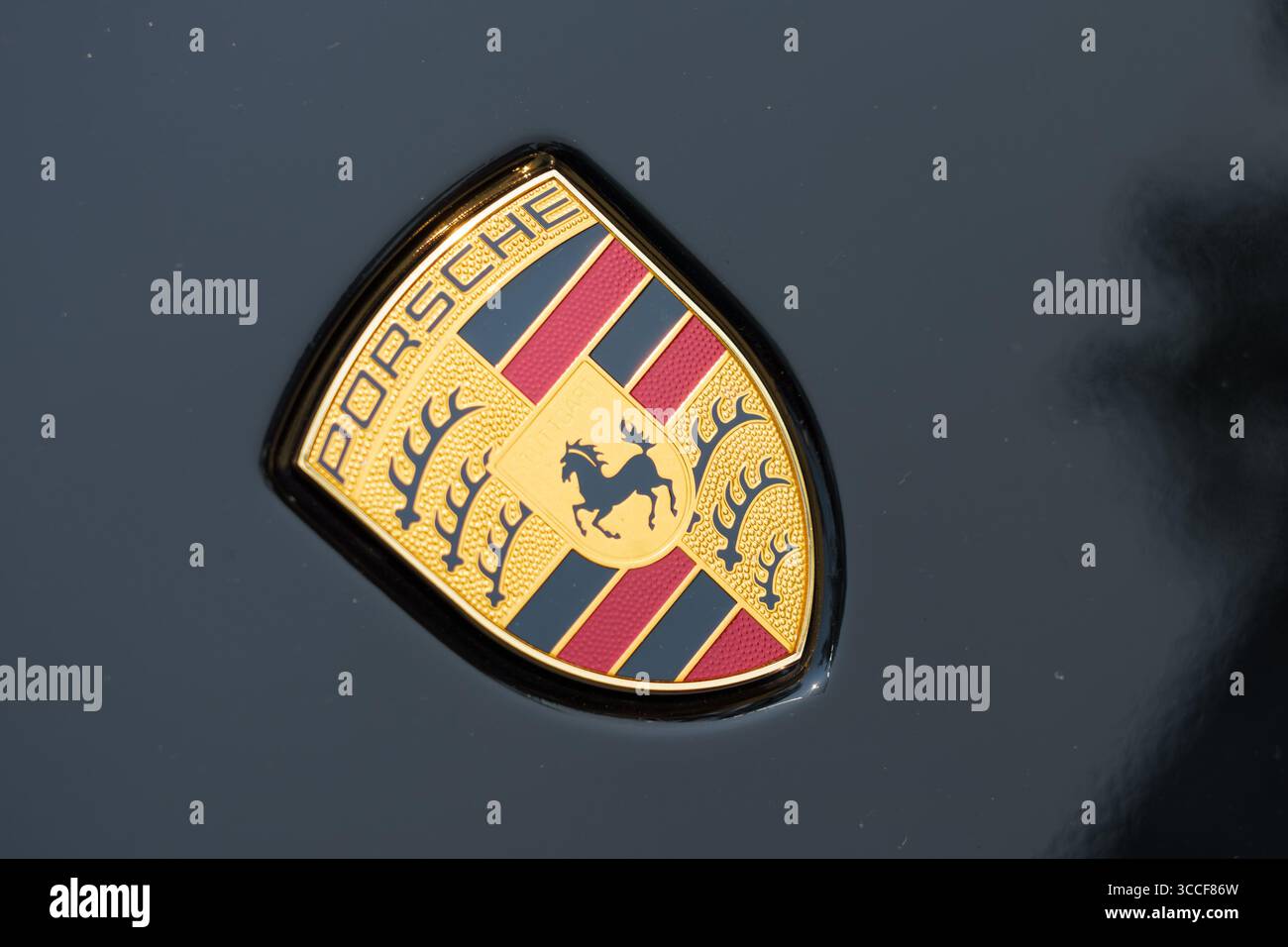 Primo piano del logo Porsche dorato con dettagli rossi e neri su una superficie nera lucida. Foto Stock
