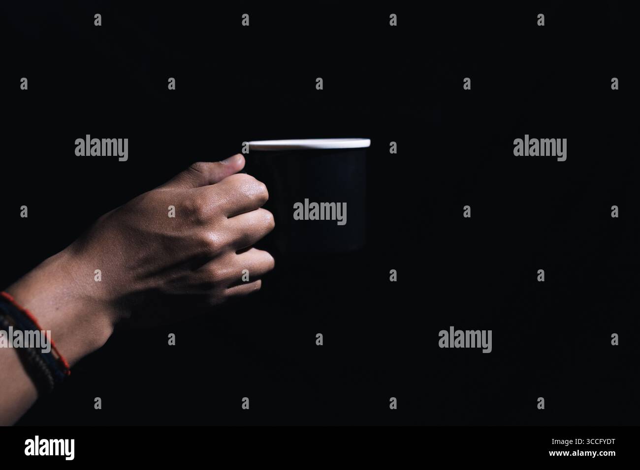 mani che reggono una tazza di caffè nero su uno sfondo nero ad alto contrasto Foto Stock