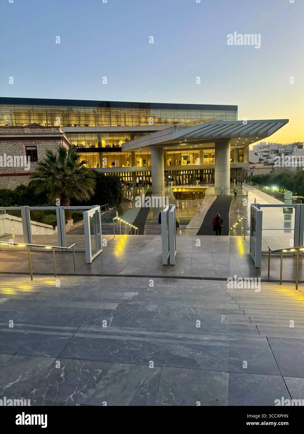 Ingresso al Museo dell'Acropoli di Atene, in Grecia, illuminato al crepuscolo con i visitatori che entrano nel moderno edificio architettonico. - Immagine stock catturata con smartphone