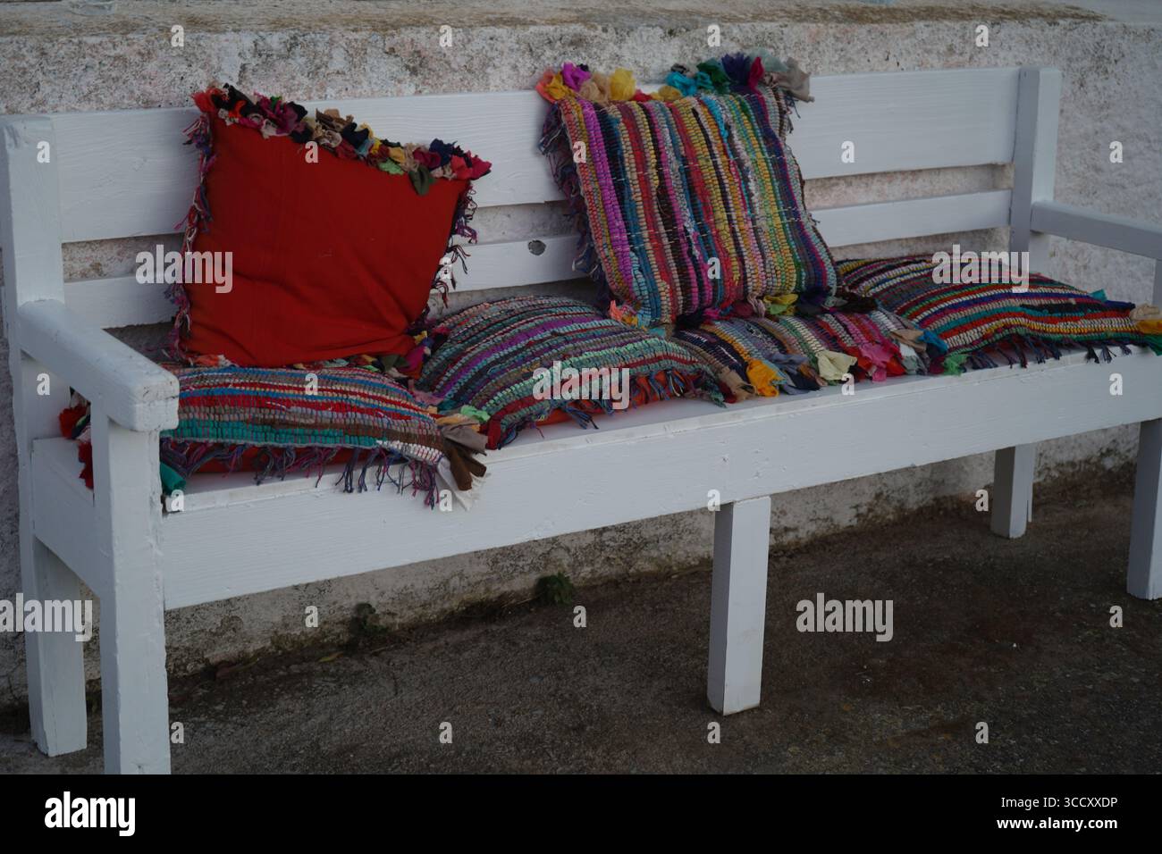 Una panchina bianca è adornata con vivaci cuscini tradizionali in tessuto cretese, che mostrano una maestria artigianale unica e un intimo stile rustico. Foto Stock