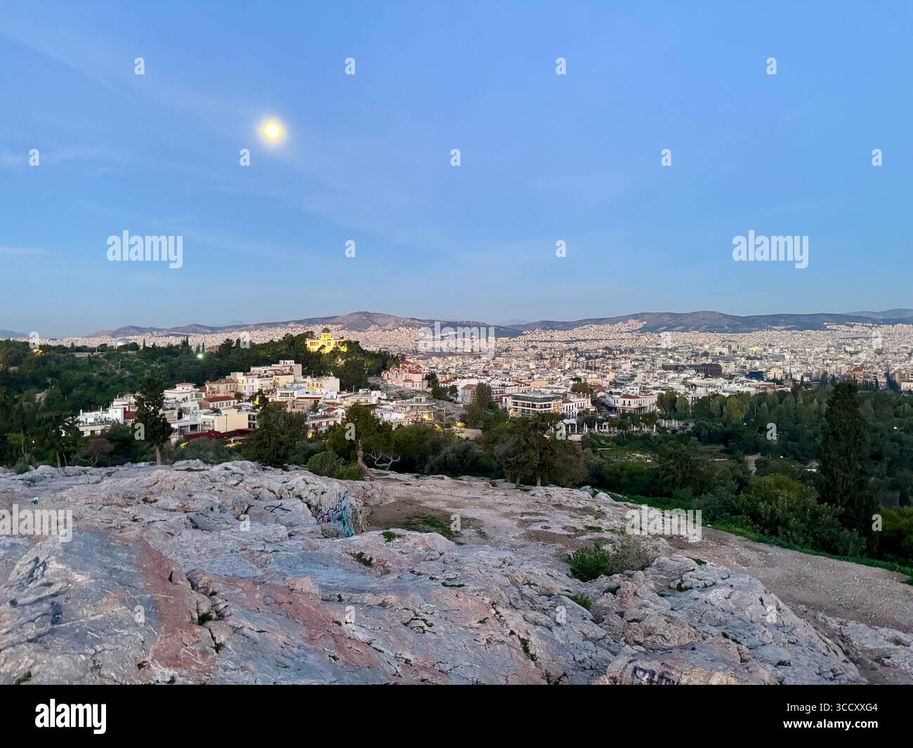 Vista panoramica della città di Atene al tramonto dalla collina di Areopago con la luna visibile in un cielo azzurro. - Immagine stock catturata con smartphone