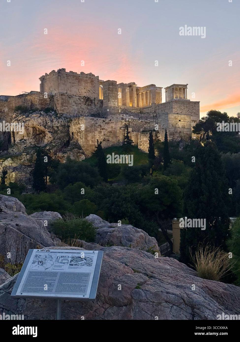 Alba all'Acropoli di Atene con una calda luce dorata che illumina le antiche rovine e una tavola informativa in primo piano. - Immagine stock catturata con smartphone