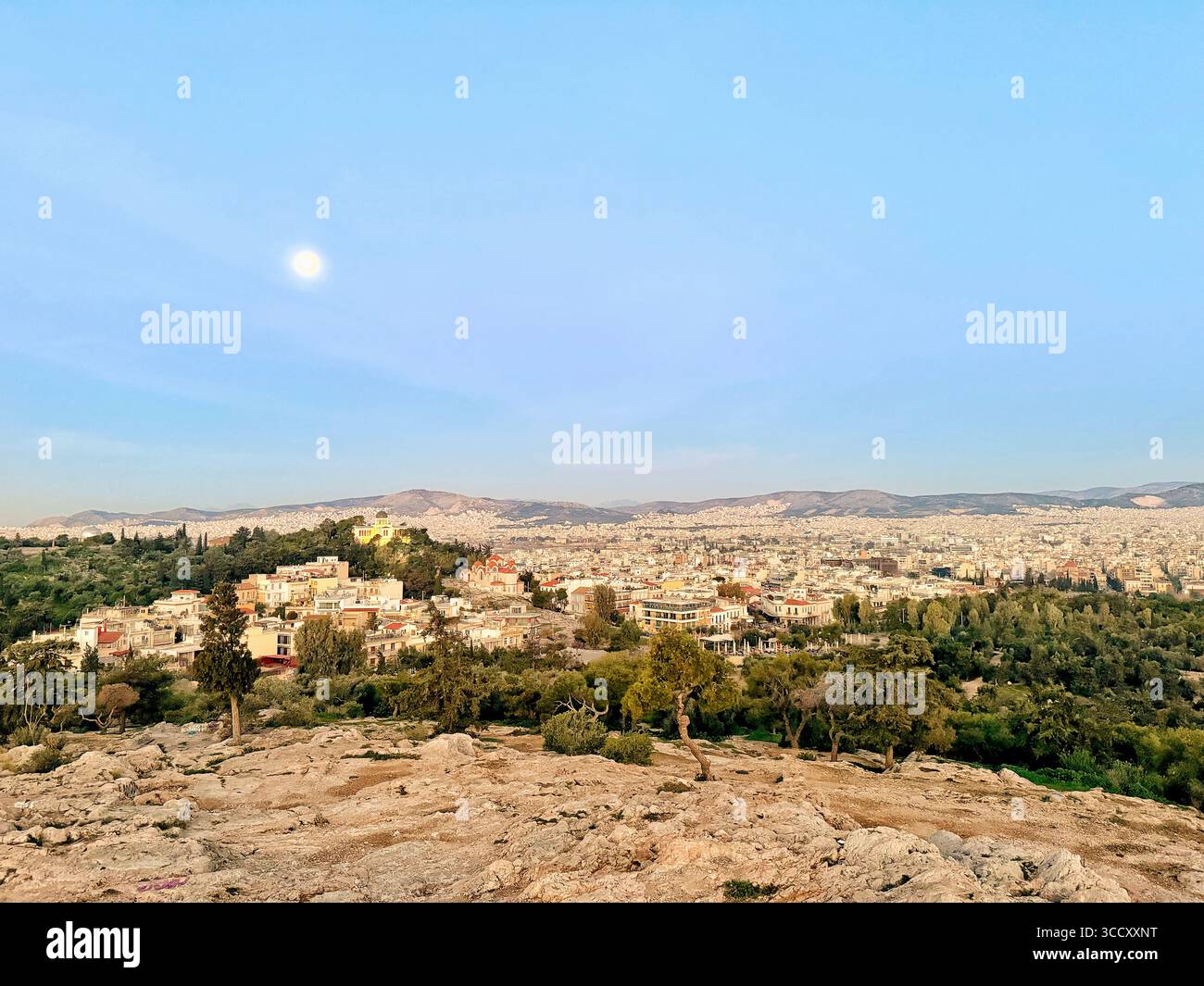 Vista panoramica della città di Atene al tramonto dalla collina di Areopago con la luna visibile in un cielo azzurro. - Immagine stock catturata con smartphone